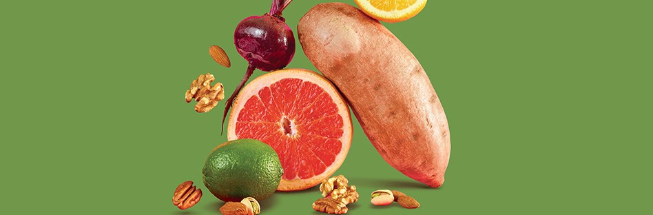 Citrus fruits, root vegetables, and nuts on a green background