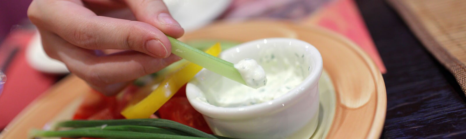 A pair of hands dipping vegetables into a cup of dip