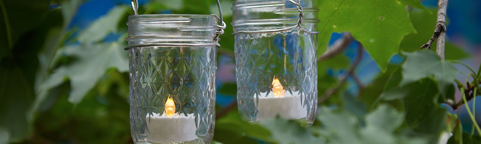 Two mason jars hanging from a tree, each one filled with a small LED candle