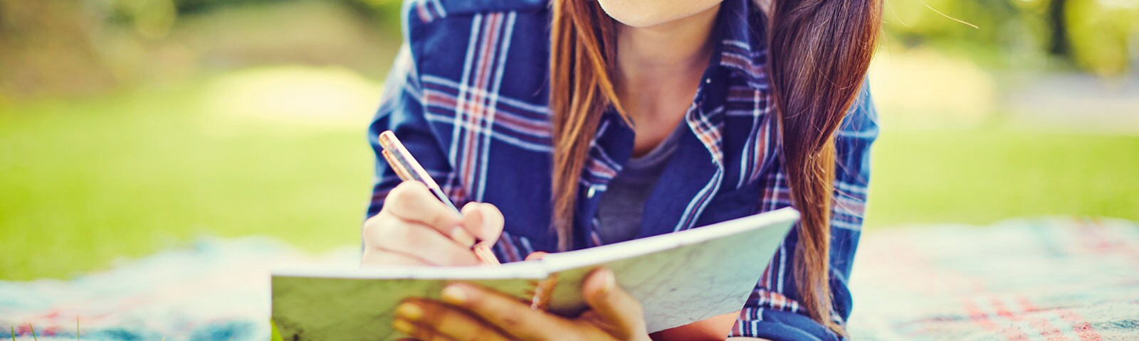 Woman laying on a picnic blanket outside in the grass writing in her journal