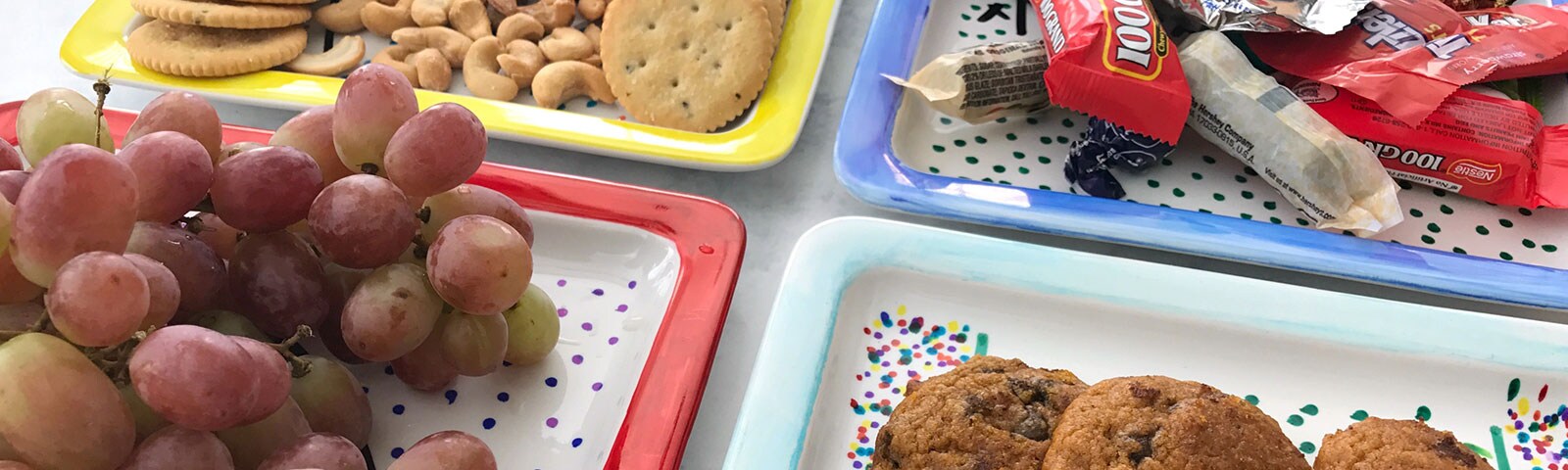 Decorated porcelain plates with a colorful polka dot design each filled with game day treats like grapes, crackers, cookies and candy