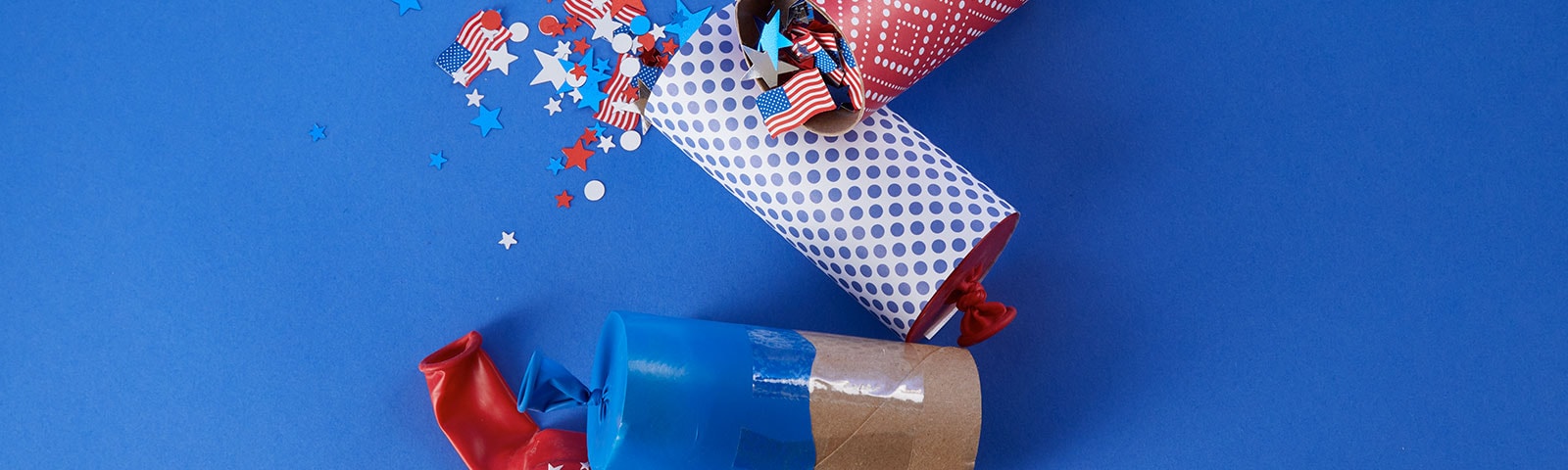 Toilet paper tubes decorated as confetti poppers with patterned paper, stickers and glitter on a blue background