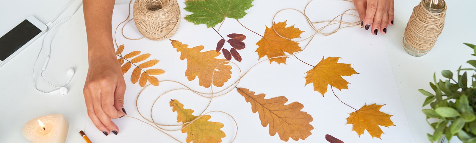 White table scattered with fall leaves, a candle, a mobile phone and twine with two hands grabbing it from each end