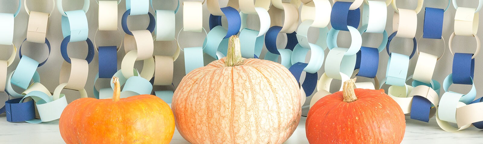Three pumpkins sitting in front of a background of paper chains in various color papers hanging from above Three pumpkins sitting in front of a background of paper chains in various color papers hanging from above