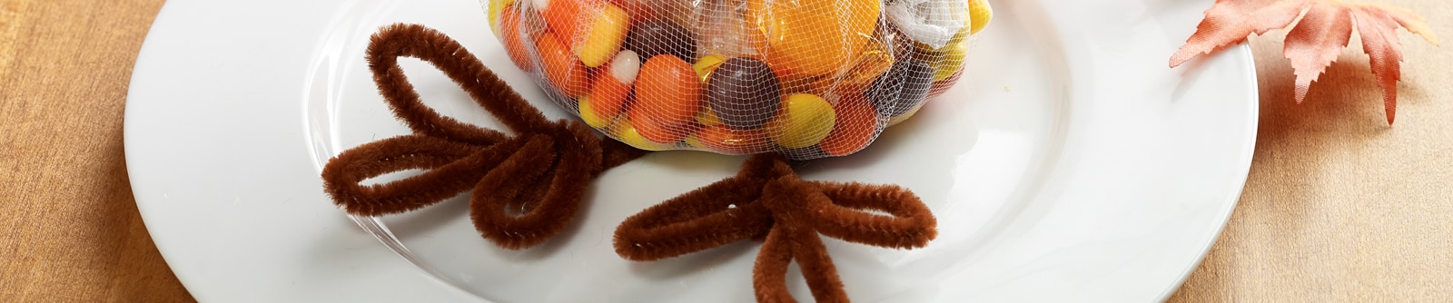 A bag of mixed candy with turkey legs made from brown pipe cleaners sit on a white plate A bag of mixed candy with turkey legs made from brown pipe cleaners sit on a white plate