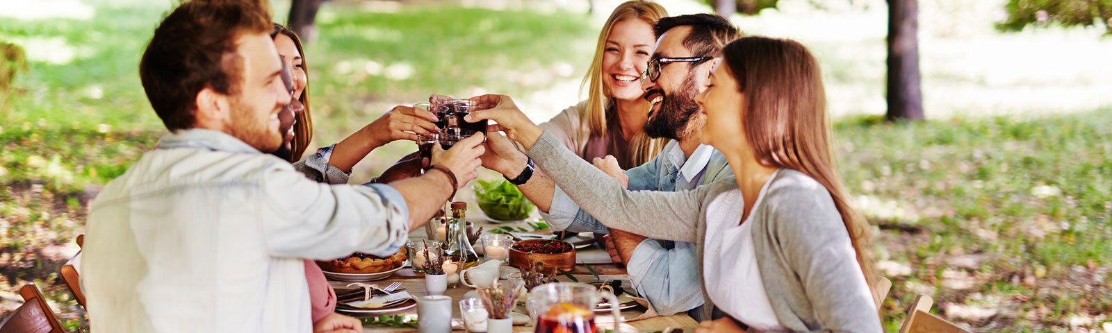 Group of friends sitting around an outdoor table sharing a friendsgiving feast and toasting one another Group of friends sitting around an outdoor table sharing a friendsgiving feast and toasting one another