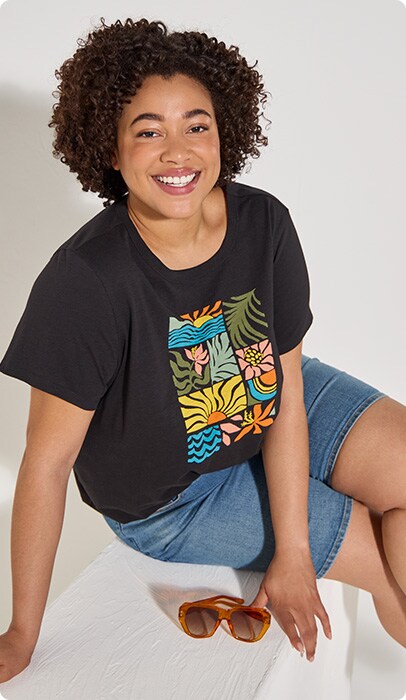 A smiling young woman with a black T-shirt with different nature patterns arranged in rectangles.